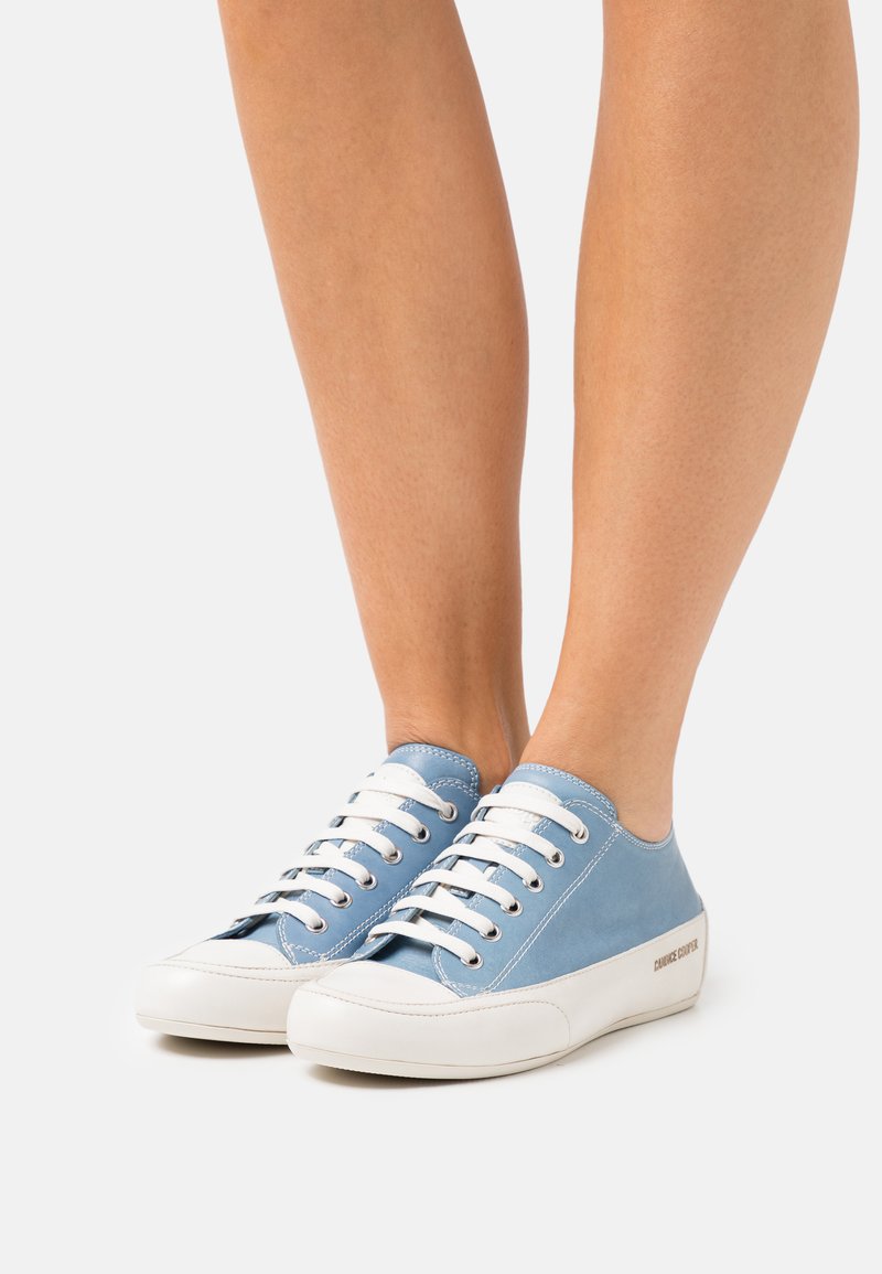 Zapatillas de lona azules con suelas de goma blanca, que cuentan con cordones blancos, ojales metálicos y un distintivo logo en contraste en el costado.