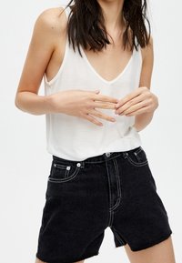 Witte mouwloze top met een diepe V-hals, gecombineerd met zwart denim shorts met hoge taille, featuring contraststiksel en een vijf-pocket ontwerp.