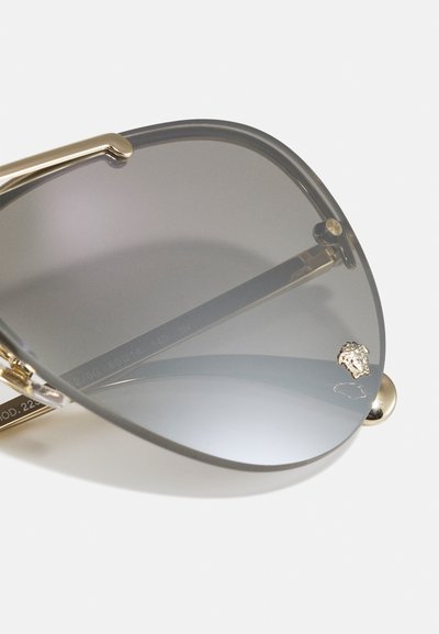 Aviator sunglasses with gradient gray lenses, gold metal frame, and lion head accent on temple. Features thin arms and glossy finish.