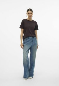 Mörkbrun t-shirt med kort ärm, parat med ljusblå vida jeans och vita spetsiga klackar, mot en enkel vit bakgrund.