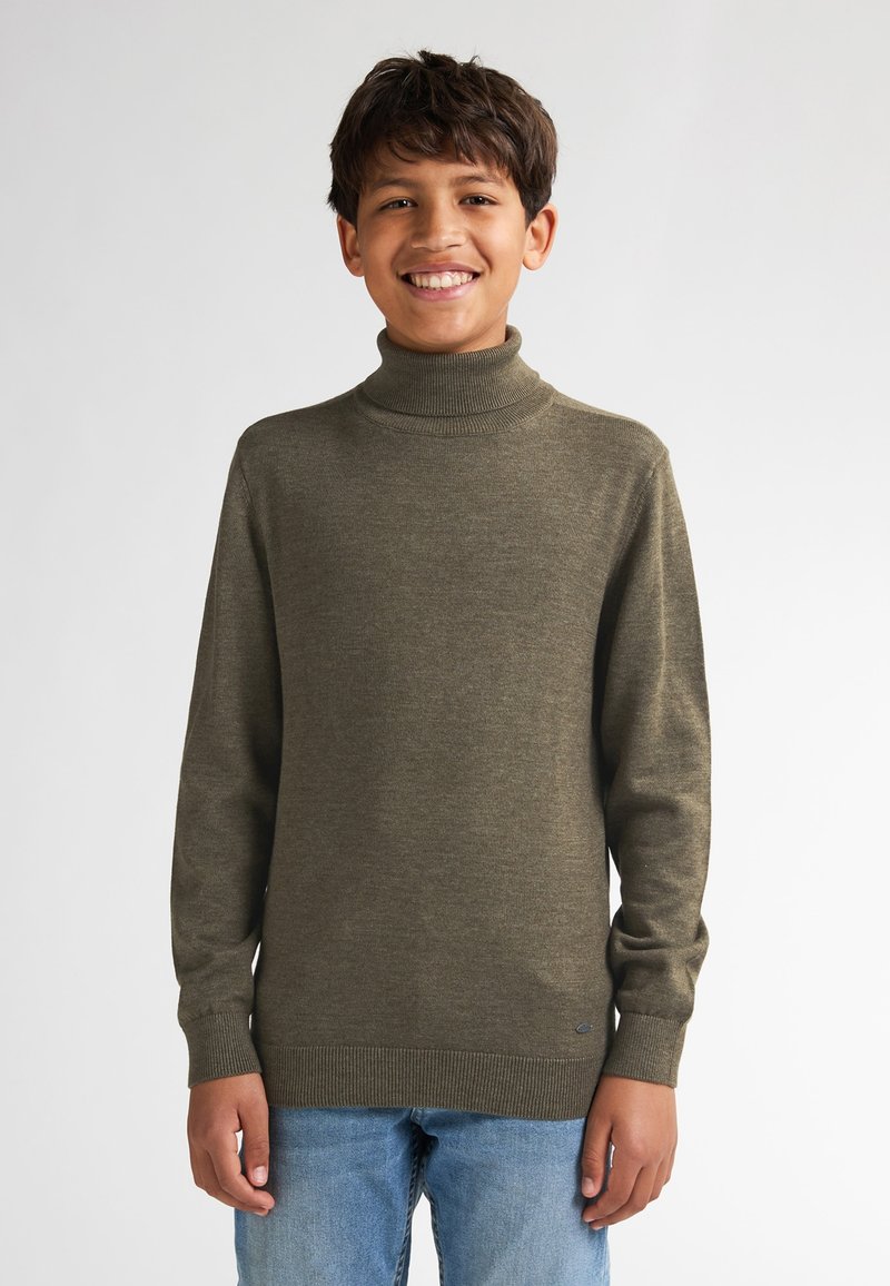 Maglione a collo alto lavorato a maglia in verde oliva, con maniche lunghe e polsini a coste, abbinato a jeans blu chiaro. Tessuto semplice e texturizzato.