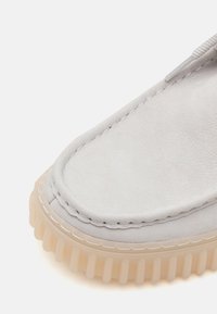 Scarpa slip-on in suede grigio chiaro con punta arrotondata. Caratterizzata da una suola in gomma testurizzata con righe e dettagli cuciti a contrasto.