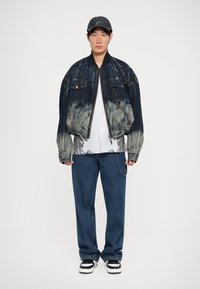 Denim jaka ar ombré efektu, melna un izbalējusi zila; valkāta pār grafisku T-kreklu. Saskaņota ar brīvām zilām džinsām un melnbaltiem sporta apaviem.