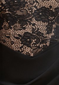 Sort blondetrøje med blomsterprint, kombineret med en glat sort stofbund. Indviklede detaljer i blondefaset og design.