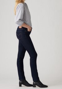 Jeans ajustados de color azul oscuro, hechos de denim, con un diseño clásico de cinco bolsillos, costuras en contraste y una etiqueta de marca en la parte trasera de la cinturilla.