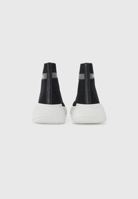 Black athletic shoes with a high mesh upper and white rubber soles. Features a grey stripe and branding on the back.