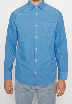 Chemise bleu clair à manches longues en tissu texturé, avec un col pointu et une poche poitrine à l'ourlet arrondi.