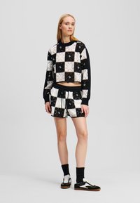 Haakstijl sweatshirt en shorts met een zwart-wit geruite patroon, met een cropped ontwerp en ribgebreide boorden. Bruin-witte sneakers.