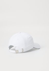 Cappello da baseball in cotone bianco con visiera curva, cinturino regolabile sul retro con fibbia in metallo argentato e dettagli di cucitura.