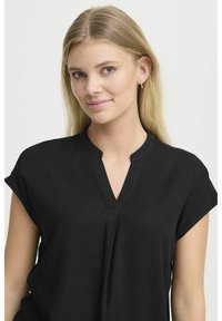 Blusa nera a maniche corte con scollo a V e vestibilità morbida, realizzata in un tessuto morbido e testurizzato con dettagli di pieghe sottili sul davanti.