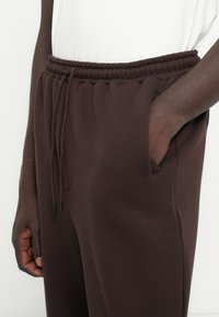 Braune Sweatpants mit elastischem Bund, Kordelzug und Seitentaschen. Glatte Textur und entspannte Passform.