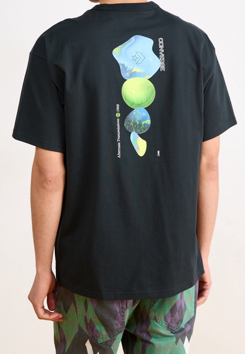 T-shirt en coton noir avec des formes abstraites multicolores au dos, incluant un globe, avec le texte "CONVERSE" au-dessus.