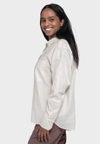 Light beige button-up shirt with long sleeves and a chest pocket. Features a smooth texture and a relaxed fit.