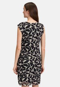 Robe à manches courtes avec un motif abstrait noir et crème, silhouette ajustée et texture transparente à l'ourlet.