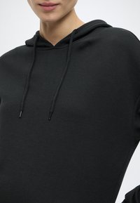 Czarna bluza z kapturem wykonana z miękkiej tkaniny, z kieszenią kangurka z przodu, regulowanymi troczkami oraz fakturowanym wykończeniem. Prosty design, bez wzorów.