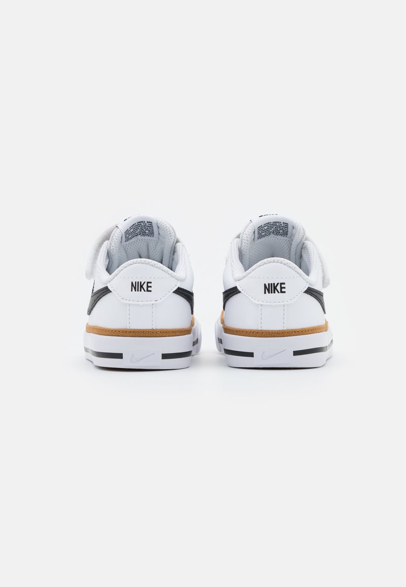 Zapatillas Nike blancas con acentos negros y una entresuela texturizada marrón. El diseño cuenta con una correa de Velcro y un collar acolchado.