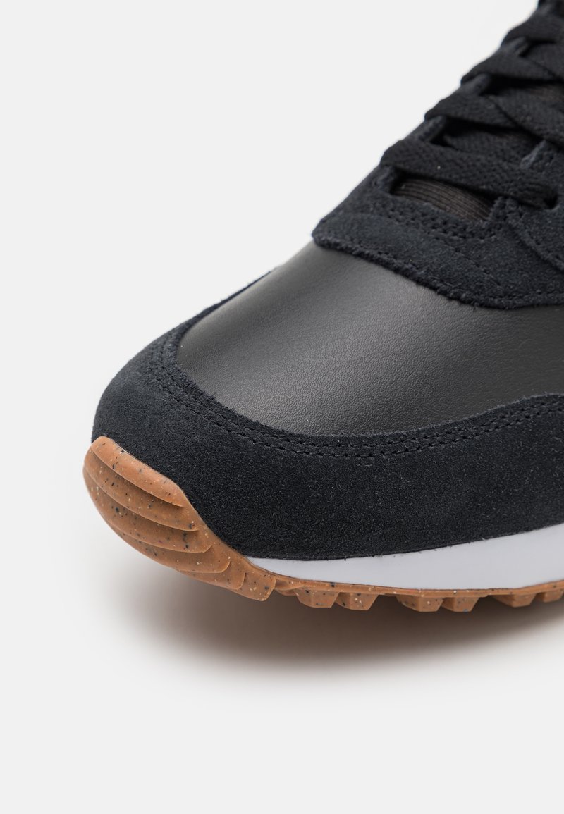 Black sneaker featuring a leather and suede upper, textured finish, and a rubber sole with a contrasting gum outsole. Laces visible.