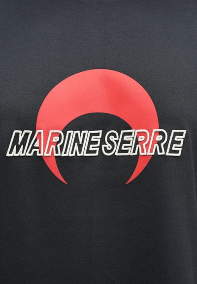 Μαύρο ύφασμα με λευκό περίγραμμα κειμένου «MARINE SERRE» πάνω σε μεγάλο κόκκινο σχήμα ημισελήνου στο κέντρο οριζόντιας διάταξης.