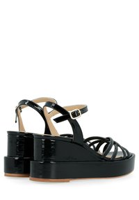 Sandales à plateforme en cuir verni noir avec des bandes entrecroisées et une boucle à la cheville. Présente une finition brillante et un talon épais.