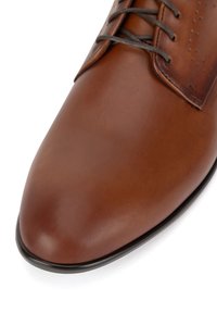 Hnědé kožené boty s hladkým povrchem, kulatou špičkou a jemnými perforacemi blízko tkaniček. Obsahují tmavě hnědé tkaničky a černou podrážku.