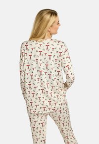 Balts pidžamas komplekts ar atkārtotu sarkano loku un zaļo lapu rakstu. Mīksts audums ar garām piedurknēm un biksēm.