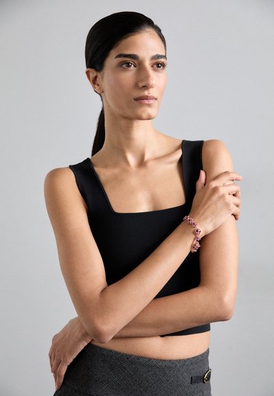 Top nero senza maniche con scollatura quadrata, abbinato a una gonna grigia con texture. Un bracciale colorato con motivi floreali adorna il polso.