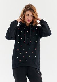 Černá mikina s kapucí s barevnými vyšívanými vzory, včetně očí, hvězd a blesků. Obsahuje stažení kapuce a volný střih.