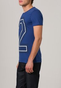 Blå bomulls-t-shirt med en stor vit siffra "2" tryckt på framsidan. Korta ärmar, rund halsringning och en slim fit-design.