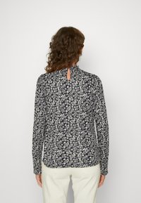 Langsleeve marineblauwe blouse met witte bloemenpatroon, opening op de rug en afgeronde zoom. Lichte stof, getailleerde silhouet.