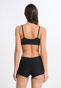 Bralette negro y pantalones cortos de talle alto a juego, hechos de un material texturizado con un brillo sutil, que cuentan con tirantes ajustables y un diseño sin costuras.