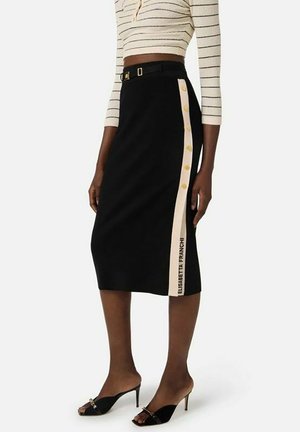 Gonna nera al ginocchio con banda laterale beige con bottoni dorati e scritta "ELISABETTA FRANCHI", abbinata a top a righe e tacchi neri.