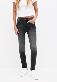 Jeans de denim negro con un diseño ajustado, cinco bolsillos y un leve desgastado. Combinados con zapatillas blancas y una camiseta blanca corta.