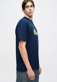 T-shirt blu navy a maniche corte in cotone, con un logo grafico colorato sulla parte frontale. Vestibilità casual con scollatura rotonda.