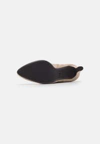 Stivale alla caviglia in suede beige con punta a punta, suola nera, zip laterale e linguetta sul tallone, mostrato dal lato della suola su uno sfondo bianco.
