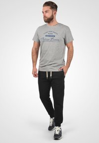 Gray cotton t-shirt with blue graphic text, paired with black joggers featuring elastic waistband and side pockets, completed with gray sneakers.