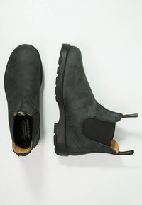 Botas de cuero negras hasta el tobillo con paneles elásticos en los lados, diseño curvado, acabado texturizado y suelas de goma. Incluyen lengüetas en la parte trasera.