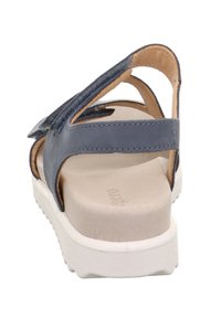 Blå lædersandal med en polstret beige inders�ål og en hvid gummisål; har krydsskinner og en udskæring ved anklen bagpå.