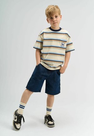 Short-sleeved, cream striped T-shirt with blue and brown lines, paired with navy cargo shorts. Styled with black sneakers and striped socks.