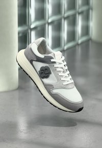 Chaussure de sport légère avec une tige en mesh blanc agrémentée d'accents en suède gris, une semelle texturée et un logo superposé unique.