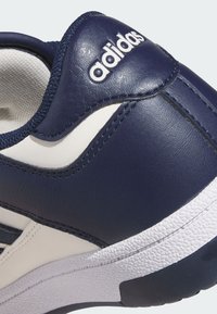 Navy modré kožené tenisky s bielymi akcentmi, štruktúrovanou gumovou podrážkou a vyšitým logom na hornej časti, s elegantným, zakriveným dizajnom.