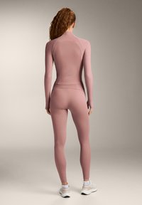 Pink long-sleeve activewear top with ribbed texture and matching high-waisted leggings. Smooth fabric, fitted silhouette, minimal branding.