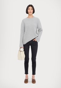 Pulover gri deschis cu borduri, blugi negri slim, pantofi slip-on maro și o geantă crem tip bucket; design minimalist cu un aspect casual.
