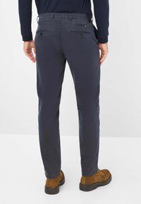 Pantaloni blu navy realizzati in un tessuto morbido, con una vestibilità slim, due tasche posteriori con chiusura a bottone, completati con scarpe in suede marroni.