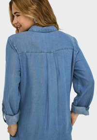 Denimskjorta i ljusblått, med krage, lång ärm med uppvikt manschett och en veckdetalj i ryggen för en avslappnad passform.