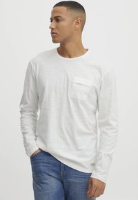 Langærmet hvid skjorte med en struktureret finish, med en brystlomme. Parret med blå denimjeans. Enkel rund halsudskæring.