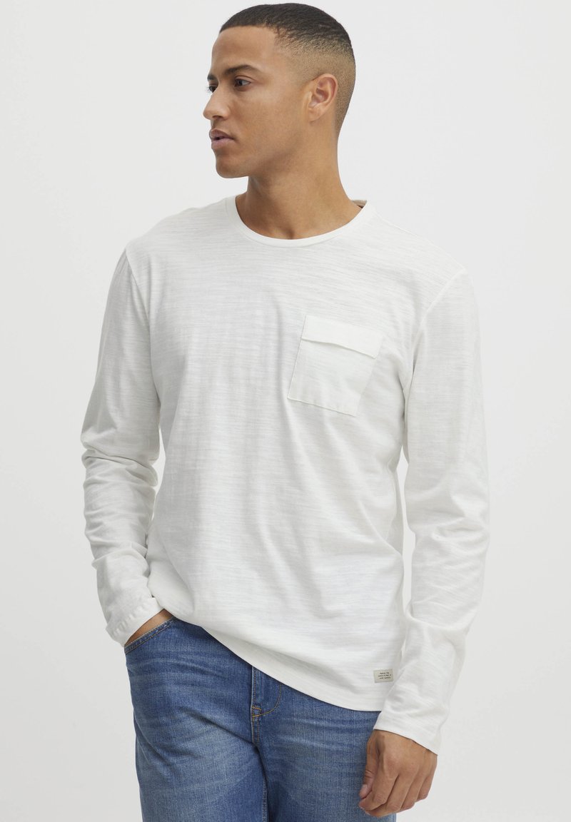 Langærmet hvid skjorte med en struktureret finish, med en brystlomme. Parret med blå denimjeans. Enkel rund halsudskæring.