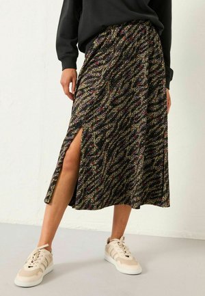 Schwarzer Midi-Rock mit buntem Blumenmuster, seitlichem Schlitz und fließendem Design. Kombiniert mit cremefarbenen Sneakers.
