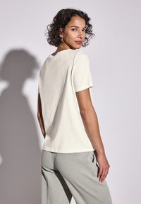 Camiseta de manga corta color beige claro con cuello redondo y un corte relajado. Material de algodón suave, con una textura lisa y un diseño sencillo.