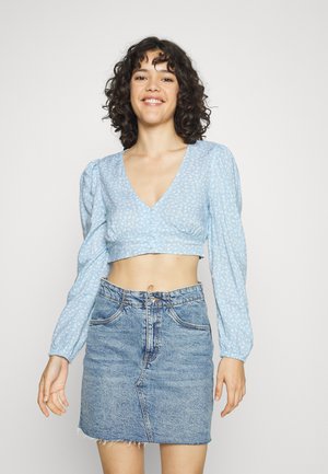Blusa curta azul clara com mangas longas bufantes e padrão floral pequeno, combinada com uma saia mini de ganga com bainha desfiada.