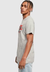 Graues Baumwoll-T-Shirt mit rundem Halsausschnitt, das auffällige rote und schwarze Grafiken aufweist. Mit kurzen Ärmeln und einem lockeren Schnitt.